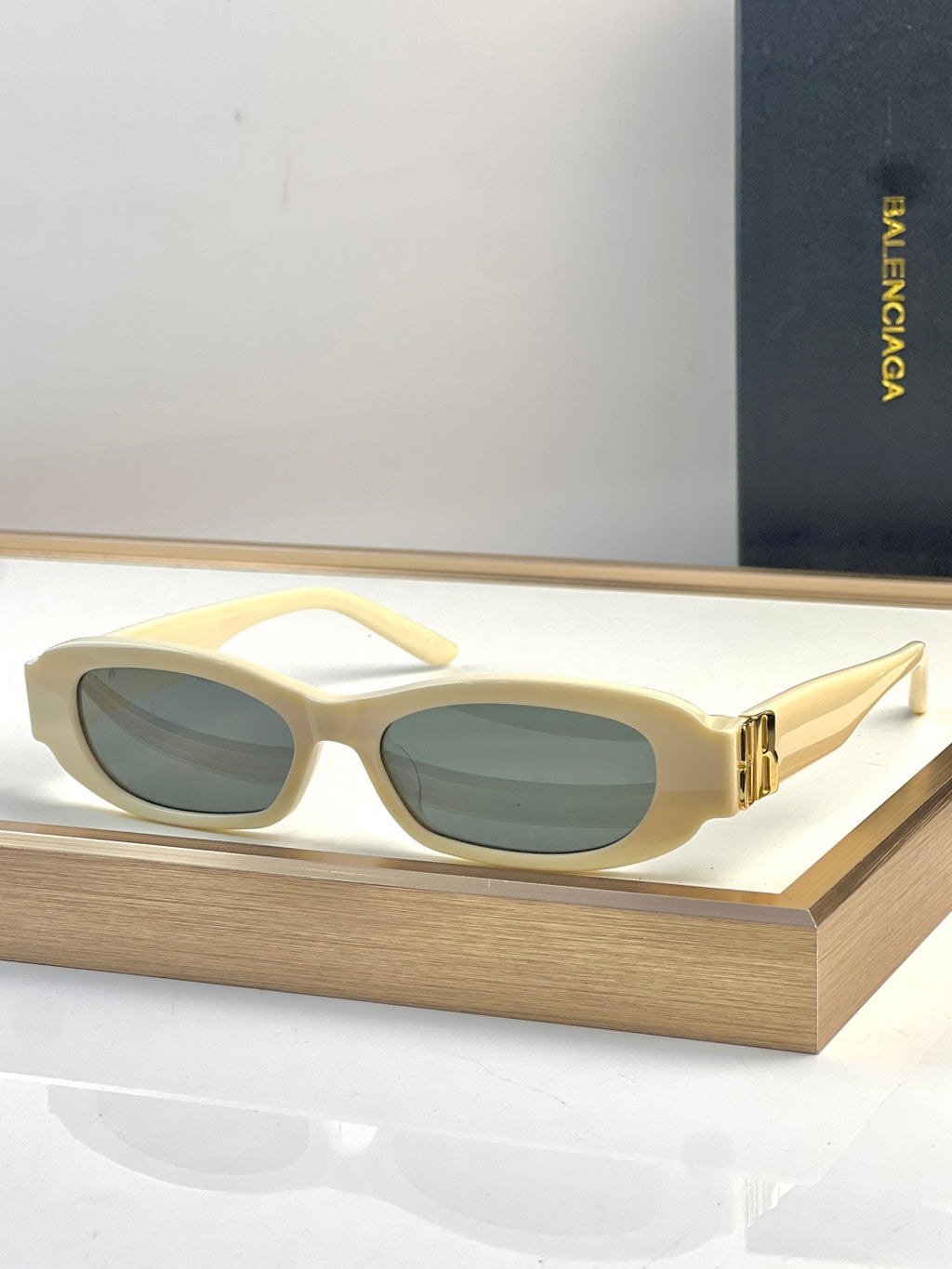 Balenciaga sunglasses with cream oval frames, green-tinted lenses, gold detail at temples.