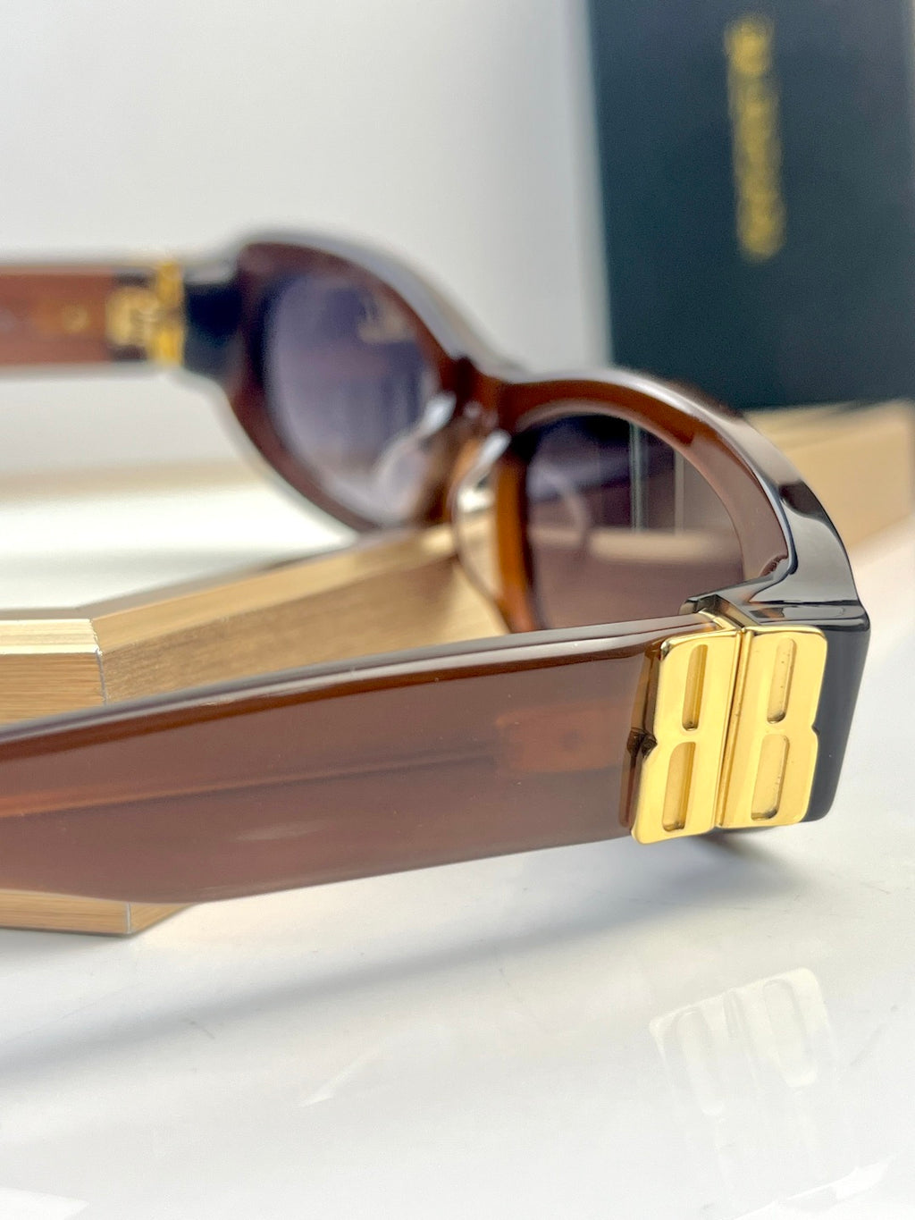 Balenciaga sunglasses close-up with brown frames, tinted lenses, and gold temple logo.