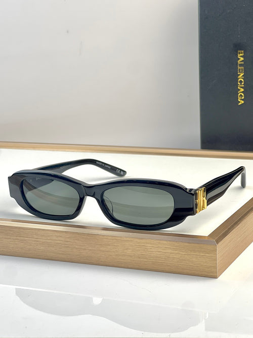 Balenciaga sunglasses with dark navy oval frames and green-tinted lenses, gold detail at temple.