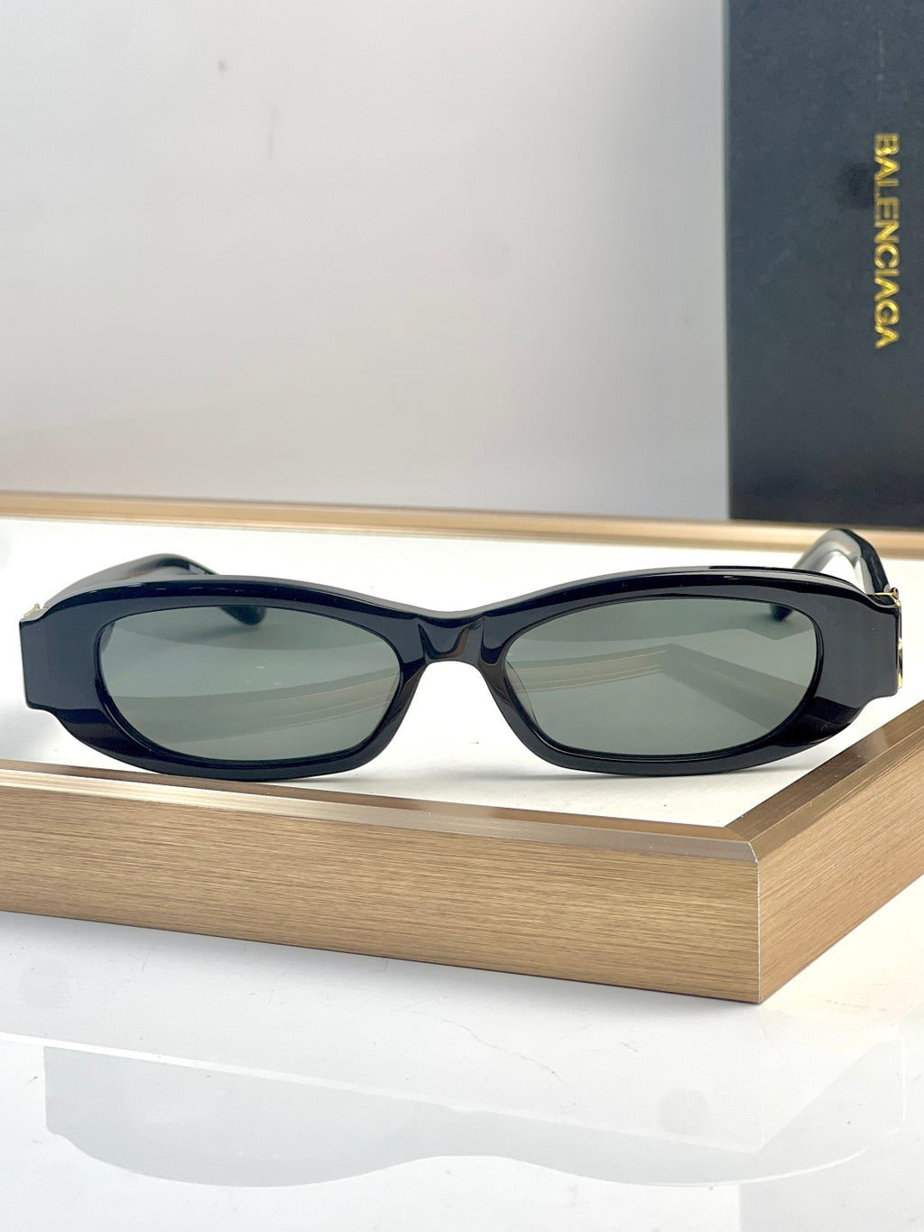 Balenciaga sunglasses with dark navy oval frames and green-tinted lenses, gold detail.