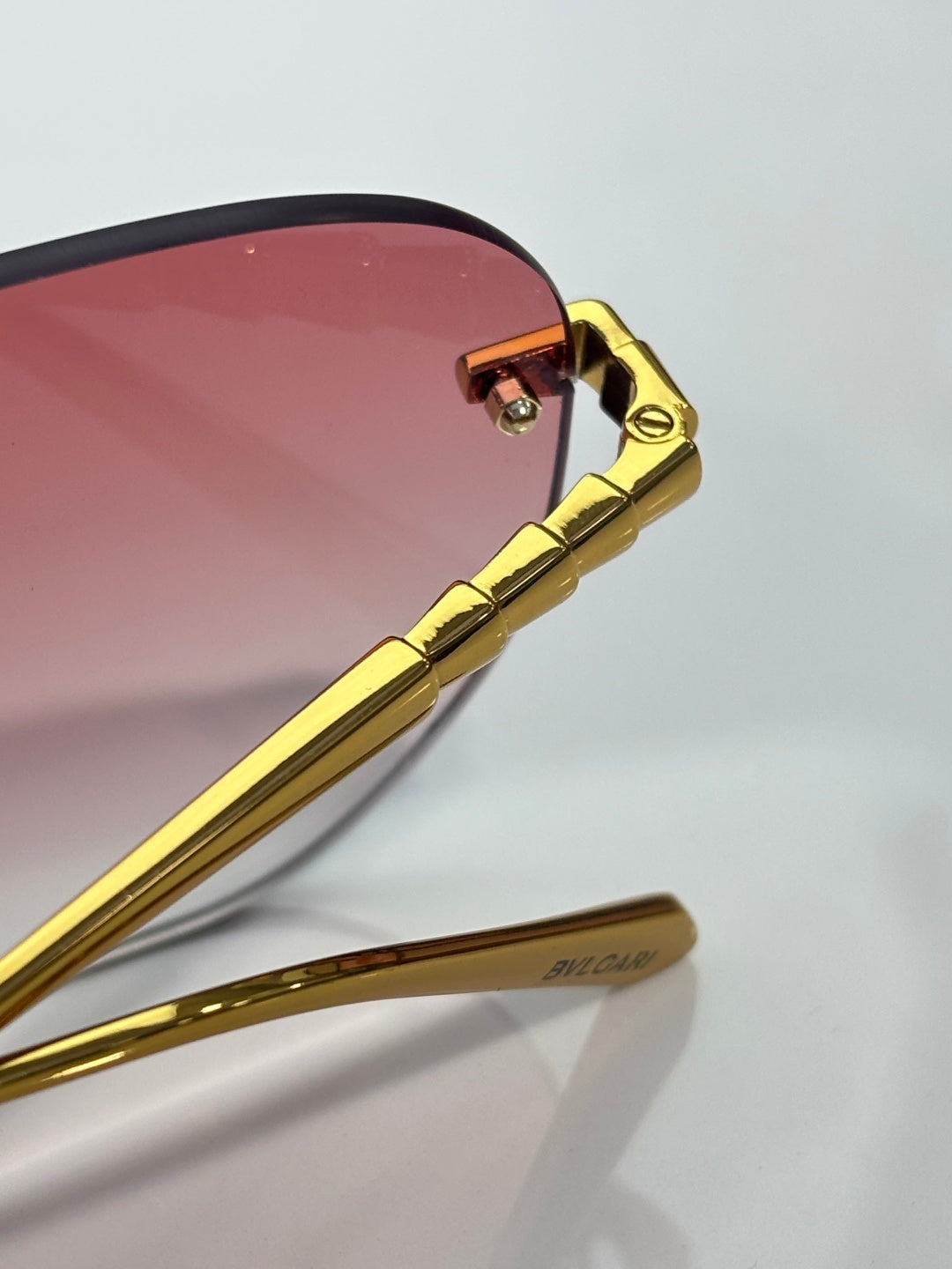 Gold metal temple and hinge on rose-tinted round sunglasses; clear lens rim.