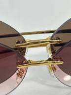 Gold-tone sunglasses bridge with tinted lenses and decorative hinge detail