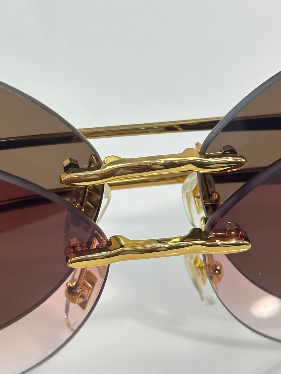 Gold-tone sunglasses bridge with tinted lenses and decorative hinge detail