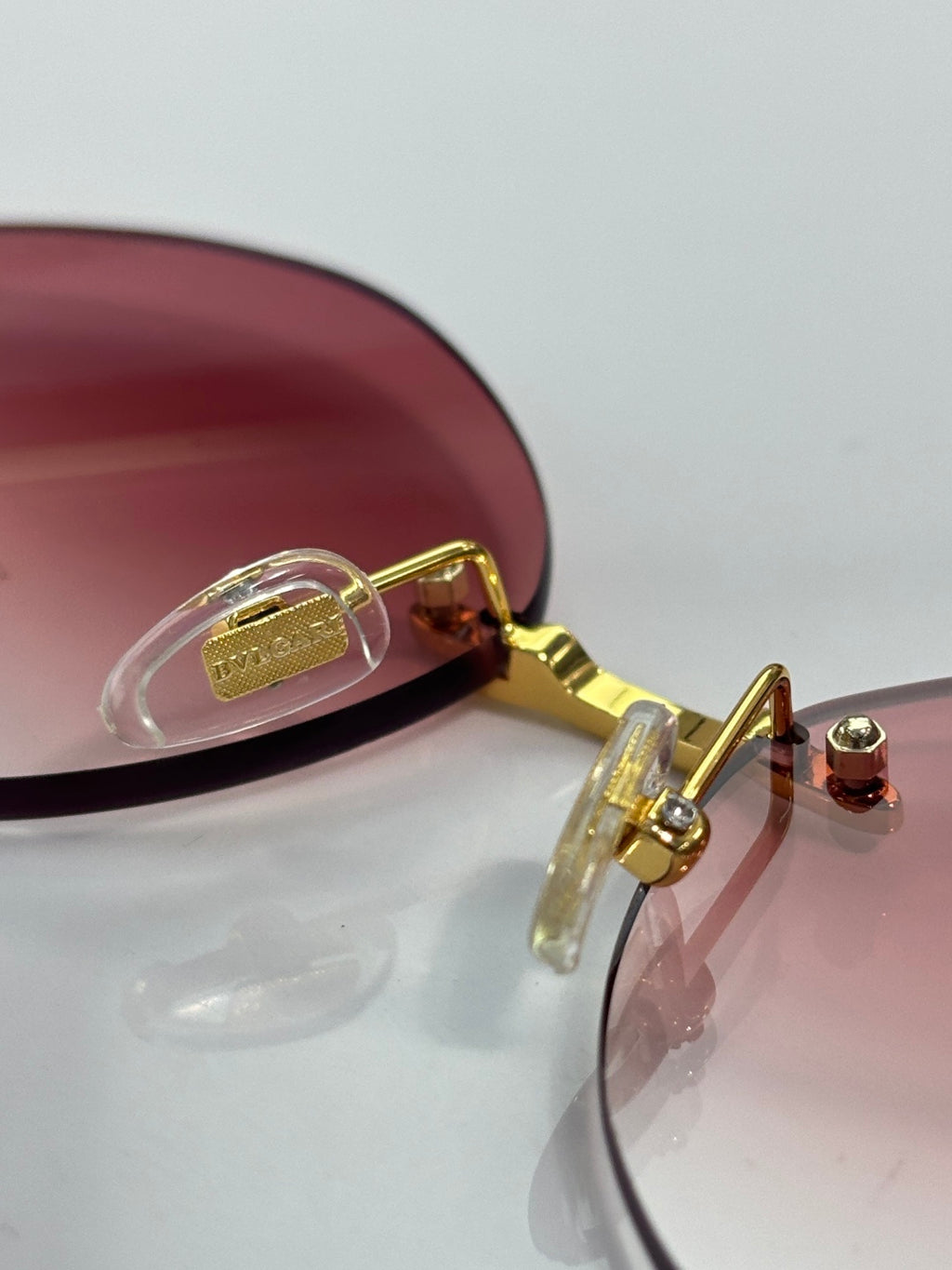 Gold-tone sunglasses hinge with engraved logo on burgundy lens frame