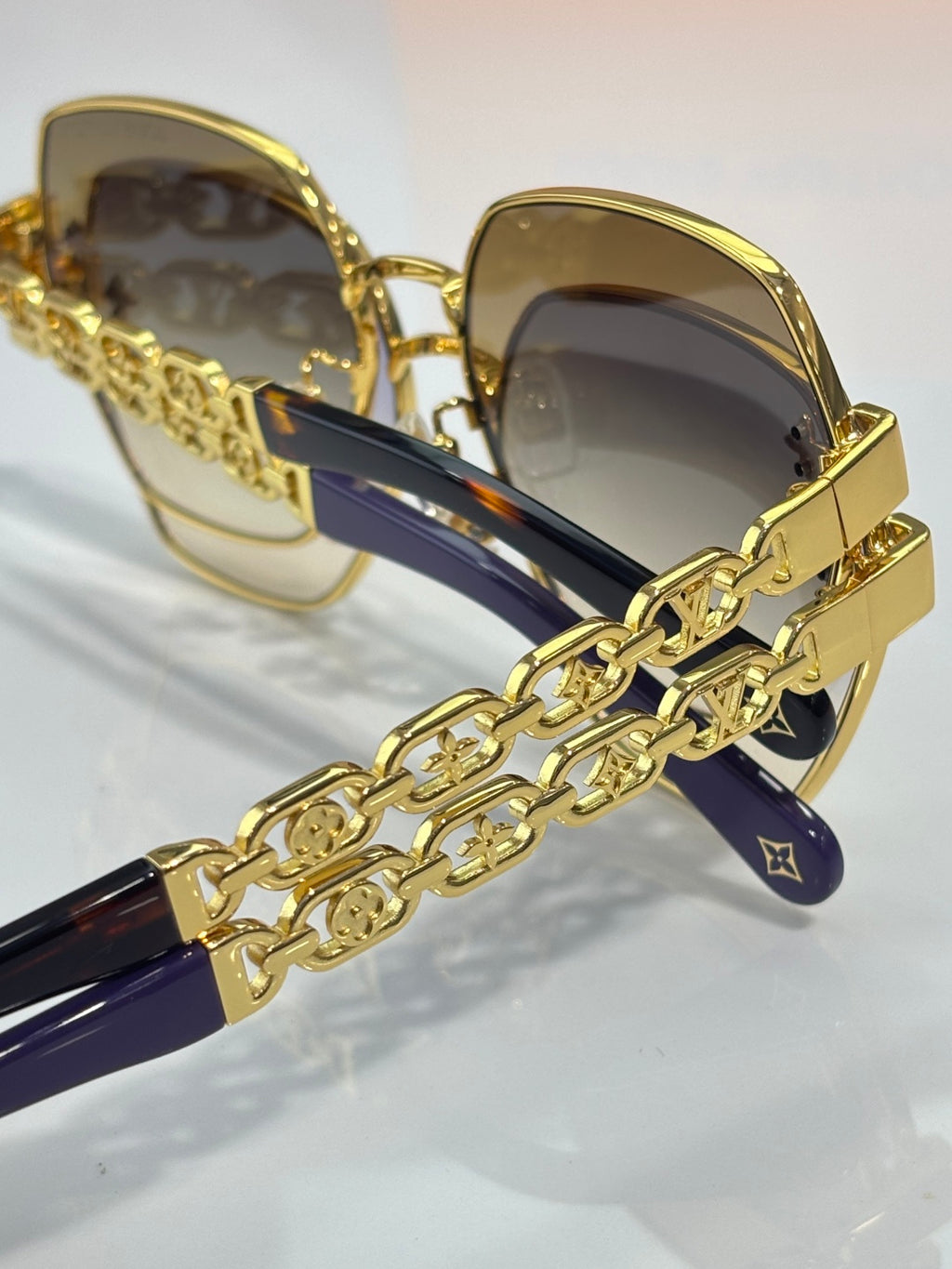 Louis Vuitton sunglasses close-up: gold frame, dark lenses, chain-link temple strap