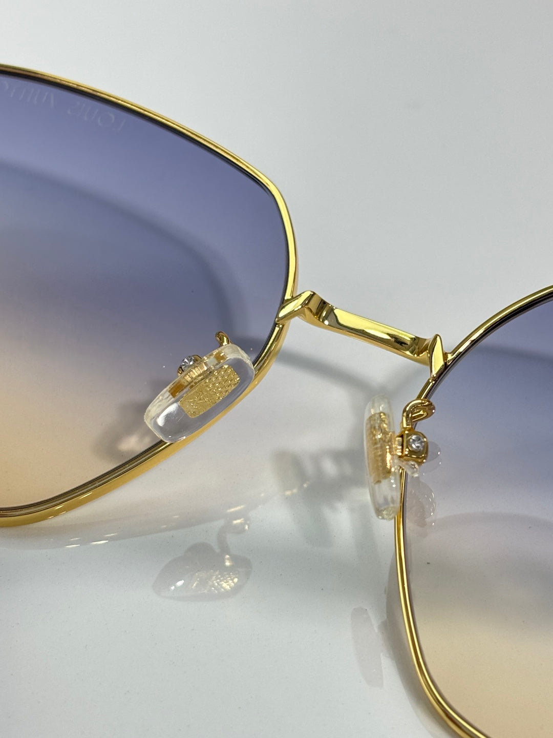 Louis Vuitton sunglasses close-up: gold-tone frame and dark lens with logo charm