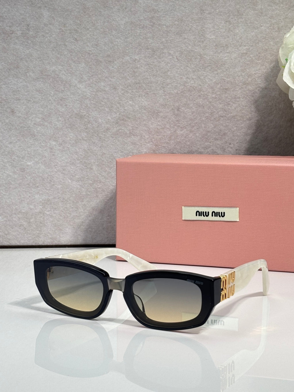 MiuMiu sunglasses with dark frames, gold side logo, and brown-tinted lenses