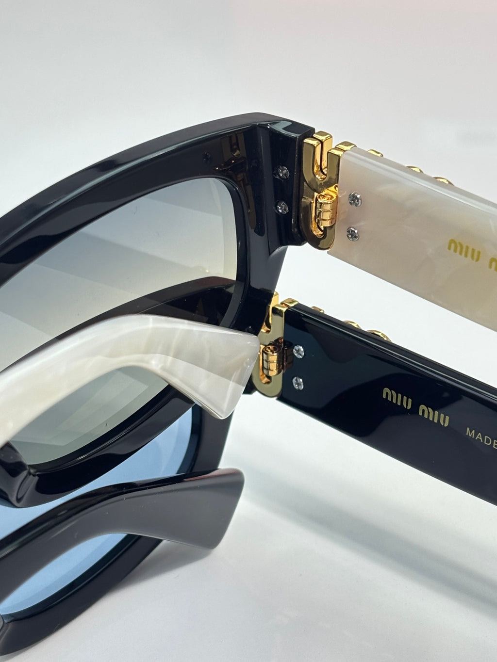 MiuMiu sunglasses close-up with gold-tone hinge hardware and dark lenses