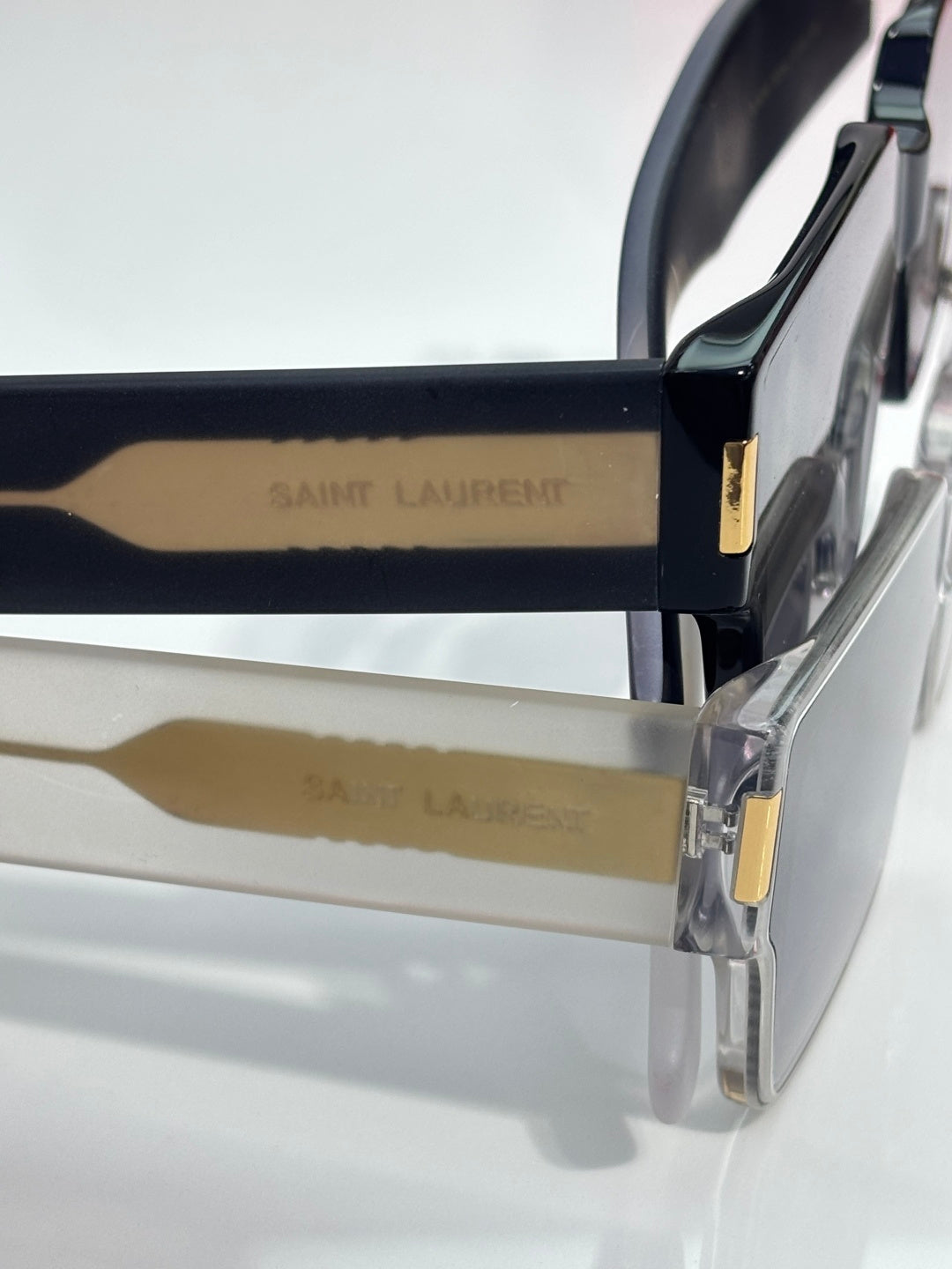 Transparent sunglasses frame with gold logo bar and dark tinted lens