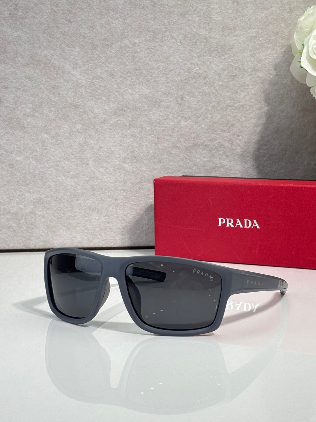 Prada sunglasses with dark lenses and black frame, next to red Prada case