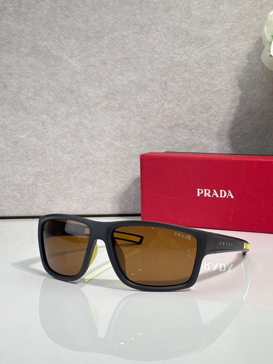 Prada sunglasses with black frame and amber-tinted lenses, with red Prada case