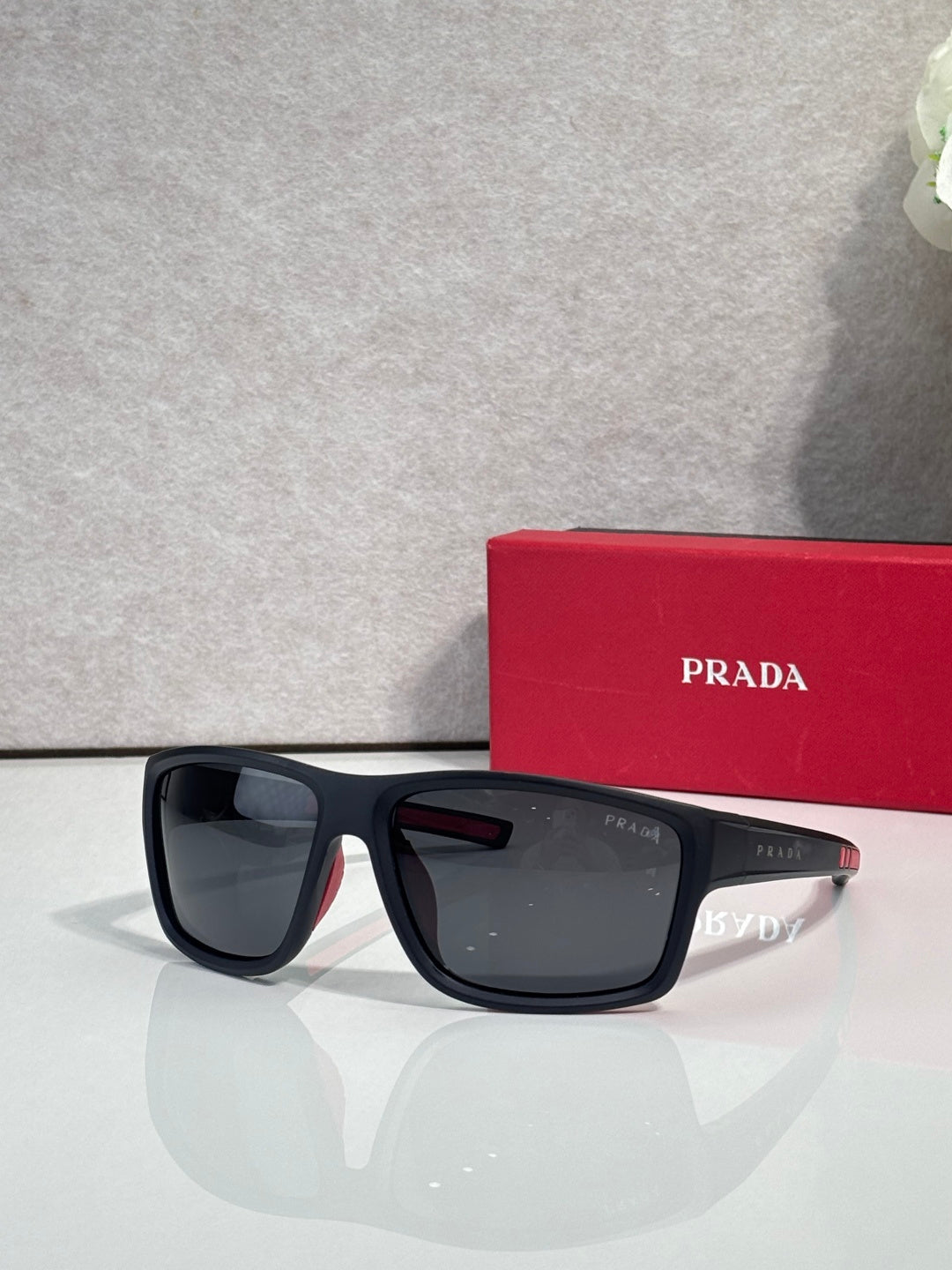 Prada sunglasses with dark lenses and black frame, beside red Prada case