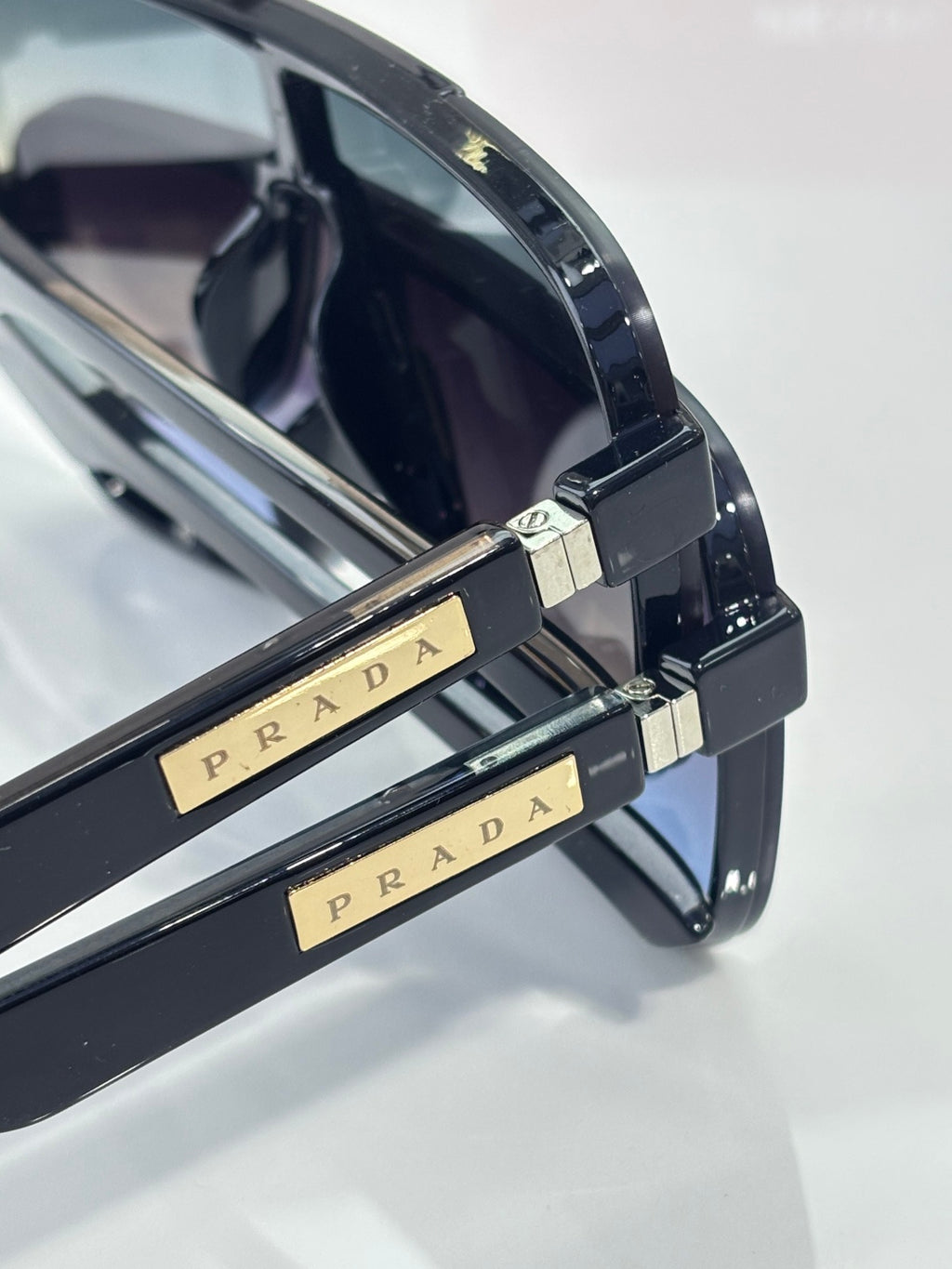 Prada glasses temple close-up with gold Prada lettering and metal hinge