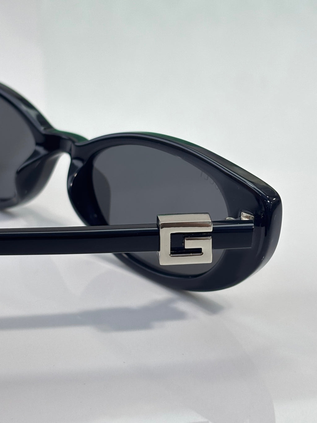 Close-up of cat-eye sunglasses hinge with gold 'G' logo on dark frame