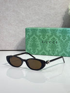 Cat-eye sunglasses with dark frames and dark-tinted lenses, gold logo hinge