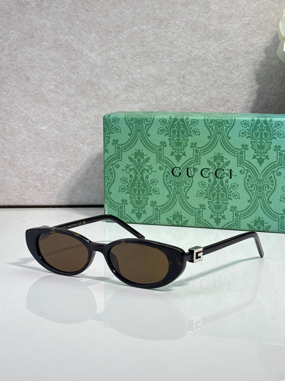 Cat-eye sunglasses with dark frames and dark-tinted lenses, gold logo hinge