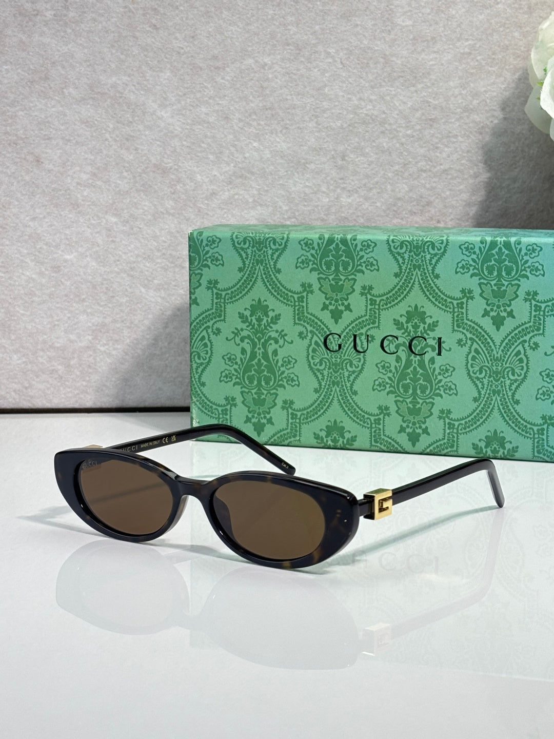 Cat-eye sunglasses with dark frames and brown-tinted lenses, gold logo hinge