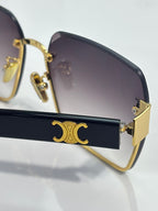 Close-up of square sunglasses: dark frame, gold monogram detail on temple