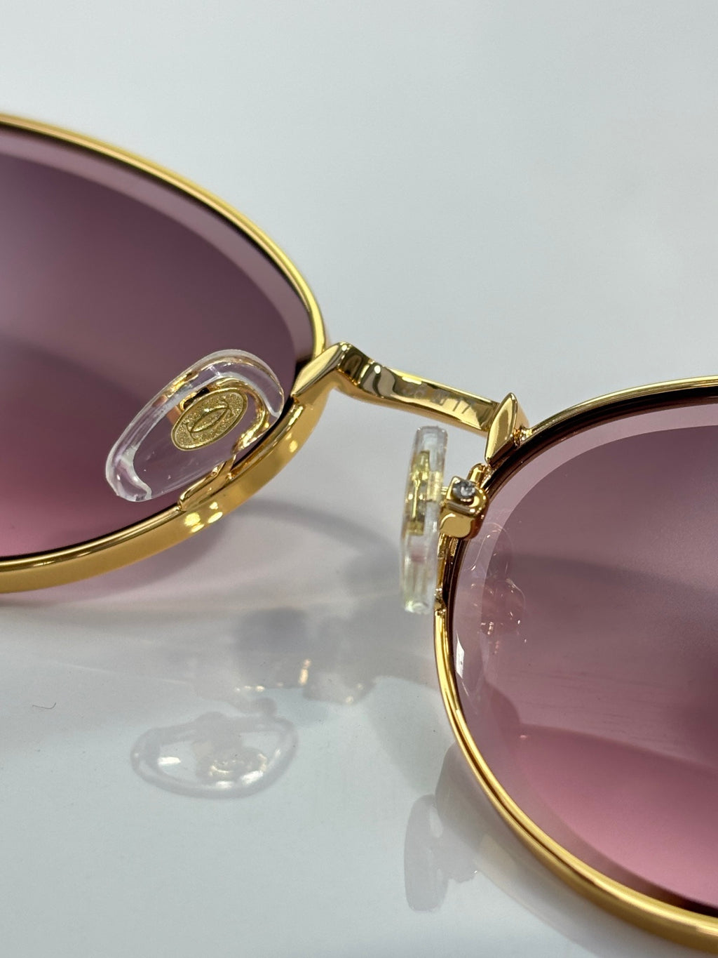 Close-up of gold-tone round sunglasses frame and pink lens