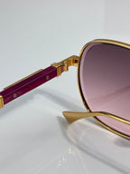 Round sunglasses with gold frame, burgundy temple, and purple-tinted lens