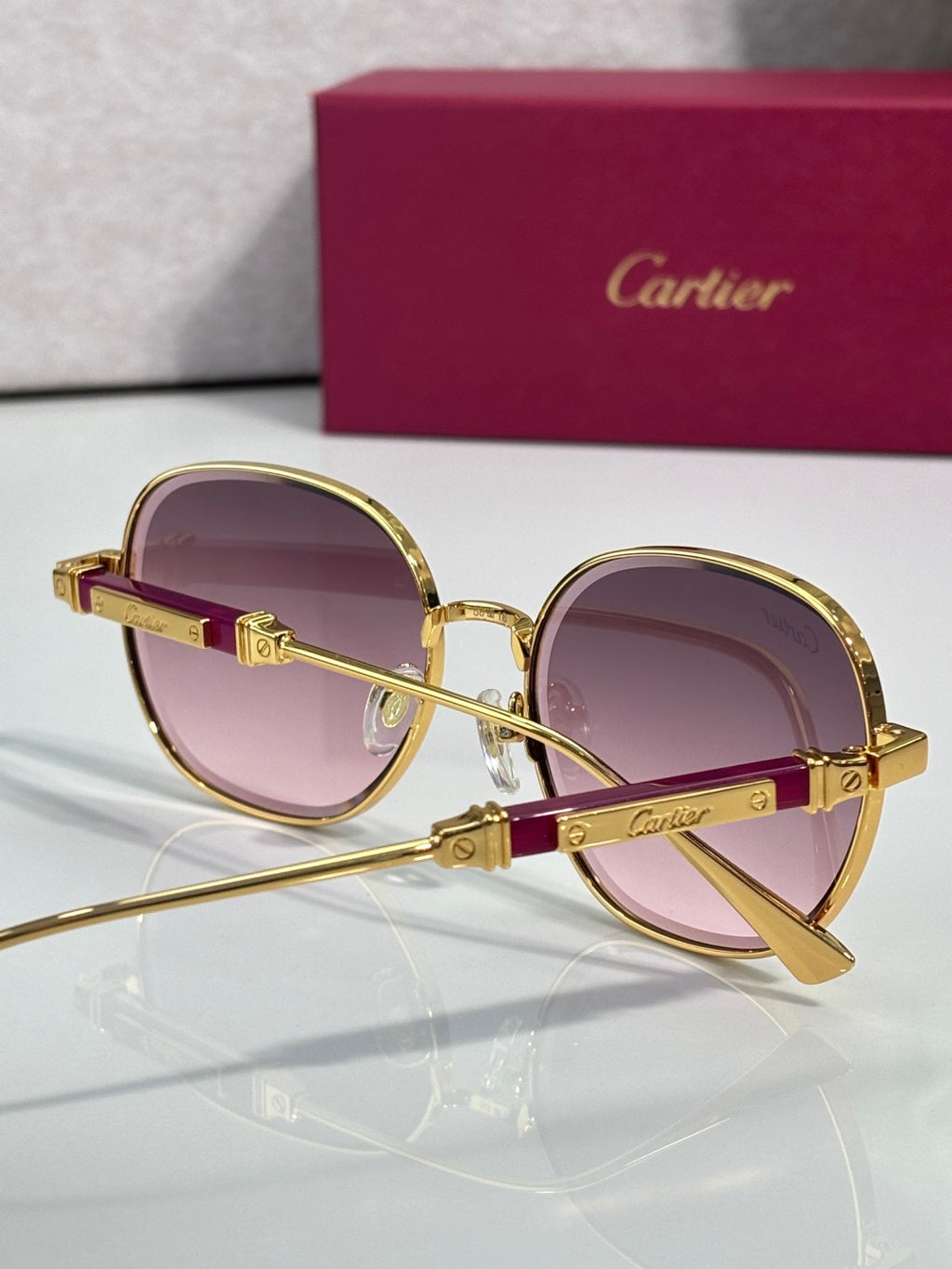 Round sunglasses with gold frame, burgundy temple, and purple-tinted lenses