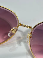 Gold-tone sunglasses close-up with purple-tinted lens and rhinestone detail