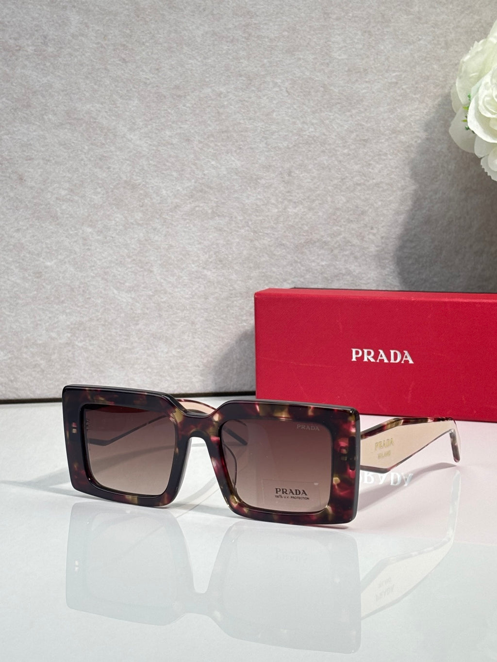 Prada sunglasses, tortoiseshell frames with dark lenses and Prada logo on lens.