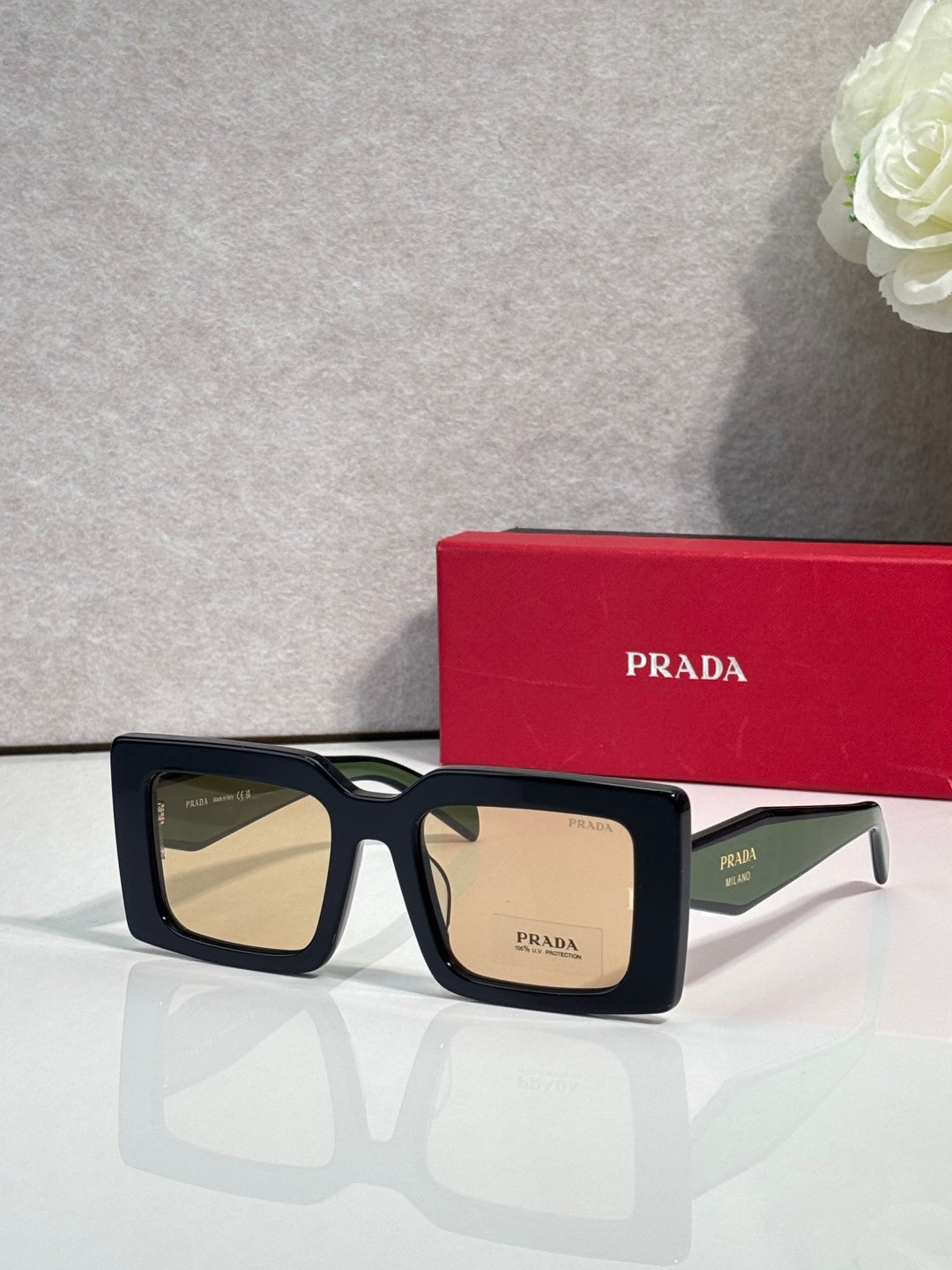 Prada sunglasses, black square frames with amber-tinted lenses and logo bridge.