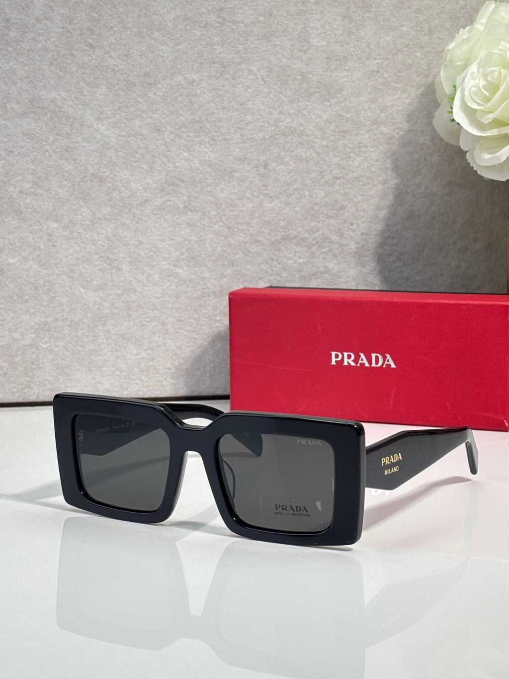 Prada sunglasses, black square frames with dark lenses in front view.