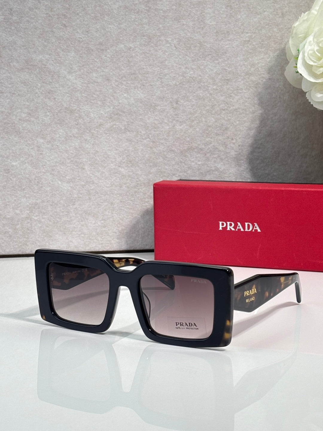 Prada sunglasses, black square frames with dark tinted lenses and Prada logo.