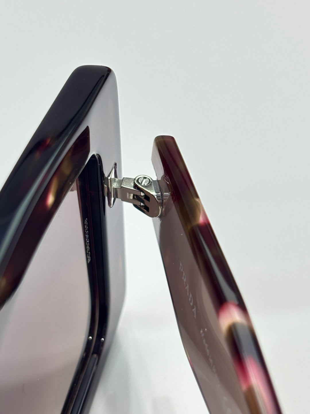 Prada sunglasses close-up: tortoiseshell temples with silver hinge hardware.