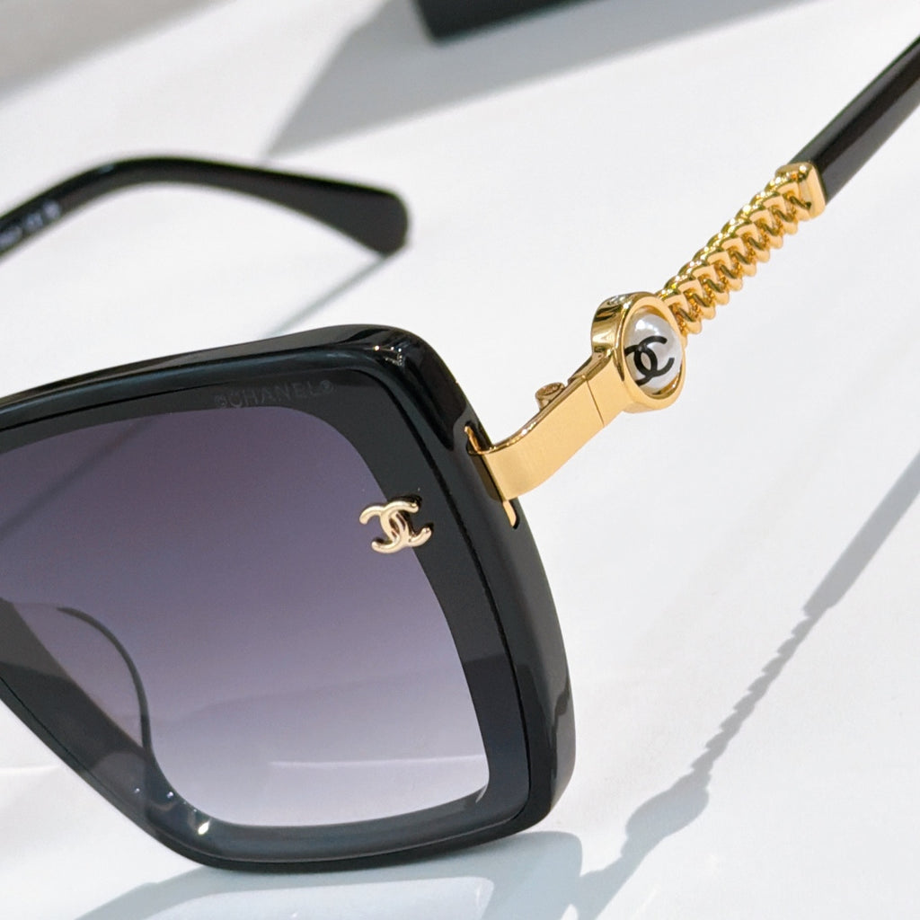 Close-up of black square sunglasses with gold chain and round logo detail