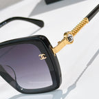 Close-up of black square sunglasses with gold chain and round logo detail