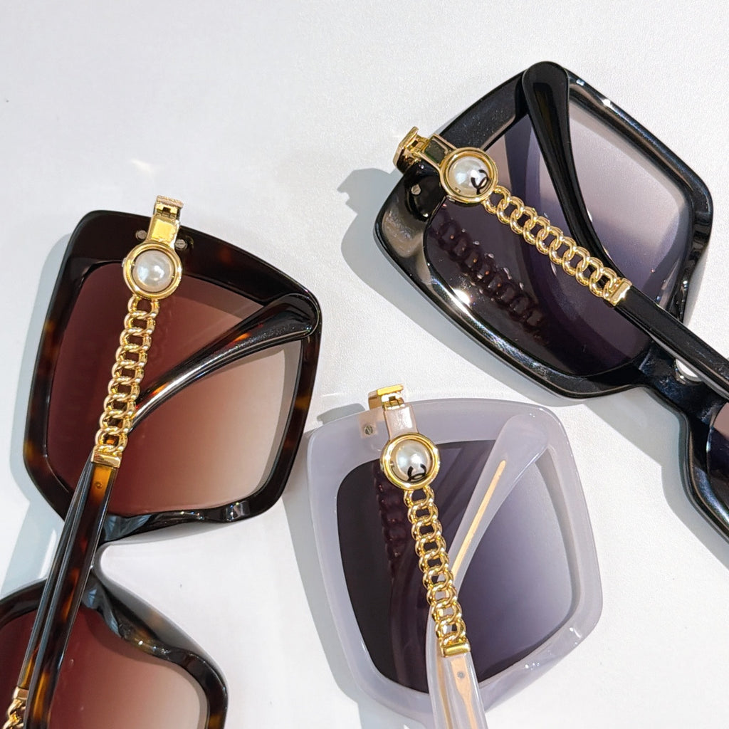 Assorted square sunglasses with gold chain temples and tinted lenses, close-up