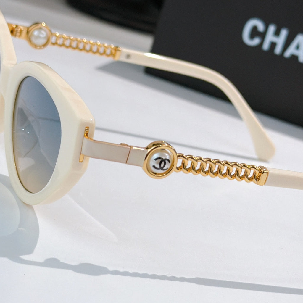 Side view of white sunglasses with gold chain arm and round emblem at hinge.
