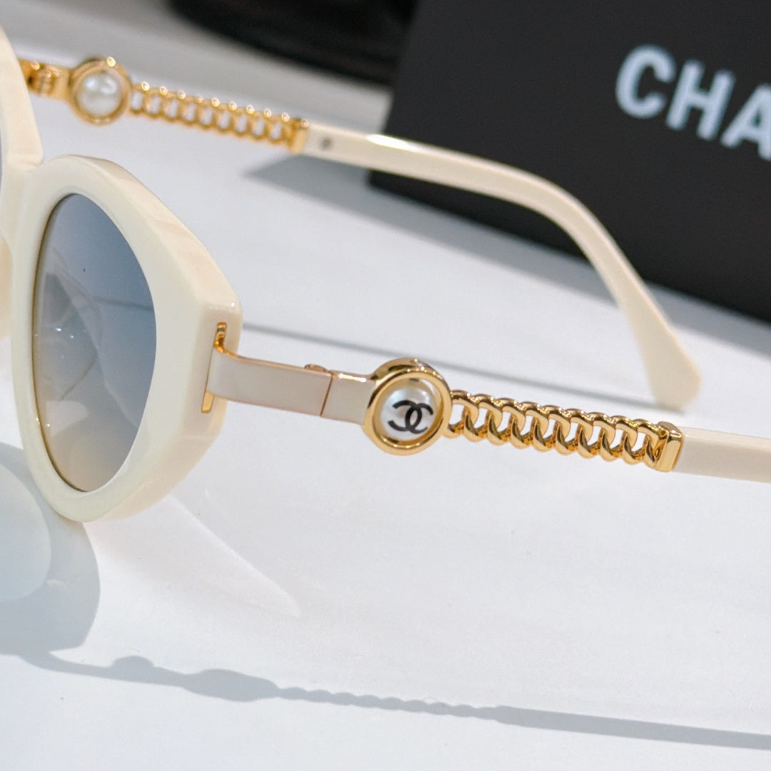 Side view of white sunglasses with gold chain arm and round emblem at hinge.