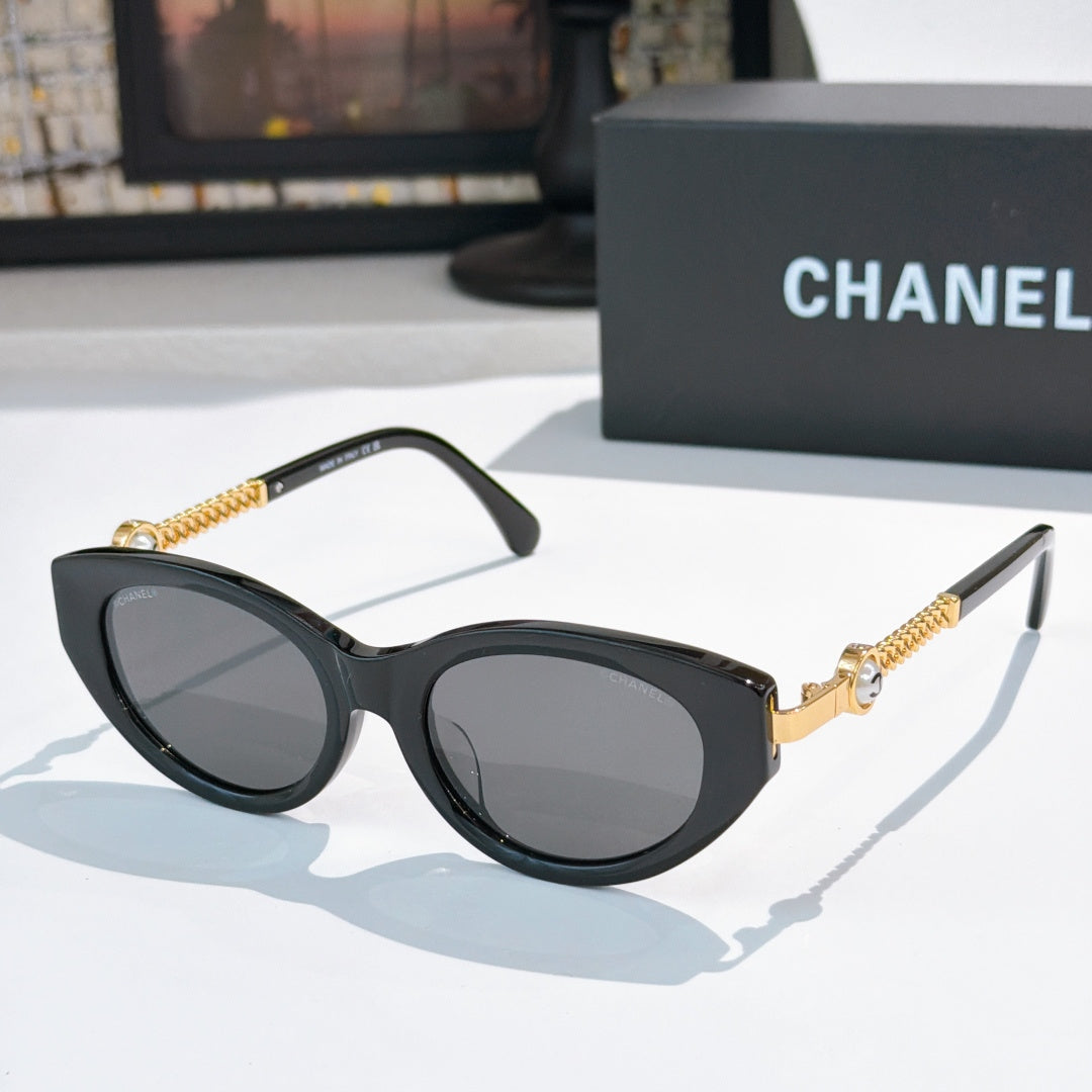 Black cat-eye sunglasses with dark lenses and gold chain detail on the temples.