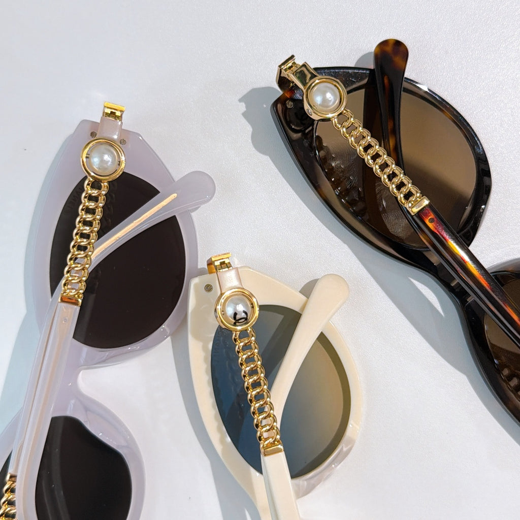 Assorted sunglasses laid flat: black and tortoiseshell styles with gold chain accents.