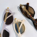 Assorted sunglasses laid flat: black and tortoiseshell styles with gold chain accents.