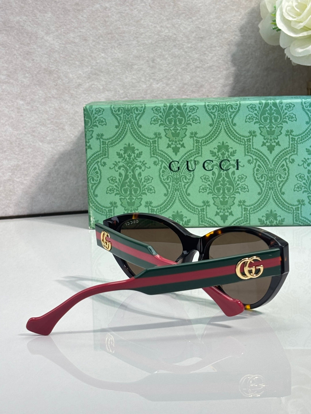 Gucci eyeglasses with black frame, green accents, and red temple tips, tinted lenses.