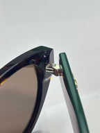 Gucci eyeglasses temple close-up with green arm and metal hinge detail.