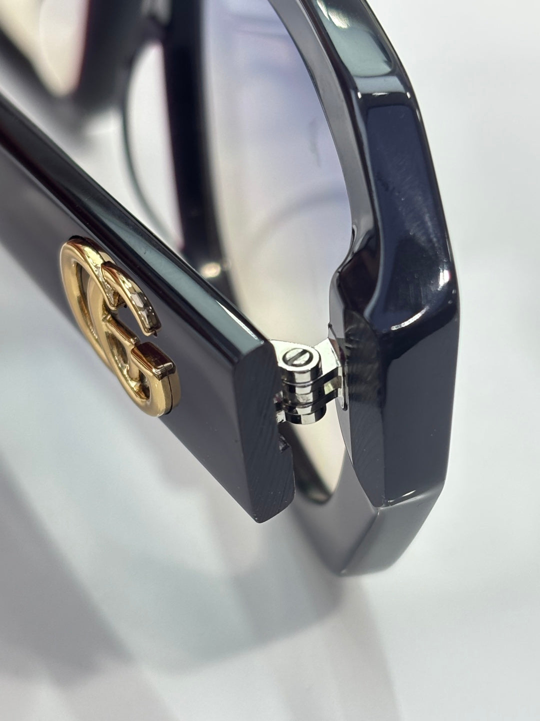 Gucci sunglasses close-up of gold logo hinge on dark frame