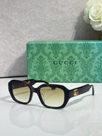 Gucci square sunglasses with dark frame, lightly tinted lenses, and gold logo temples