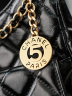 Chanel 5 round charm on gold chain over black quilted leather