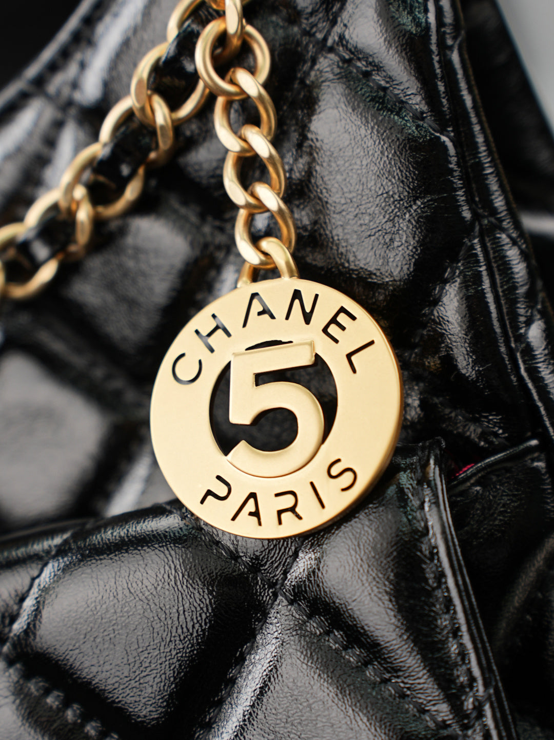 Chanel 5 round charm on gold chain over black quilted leather