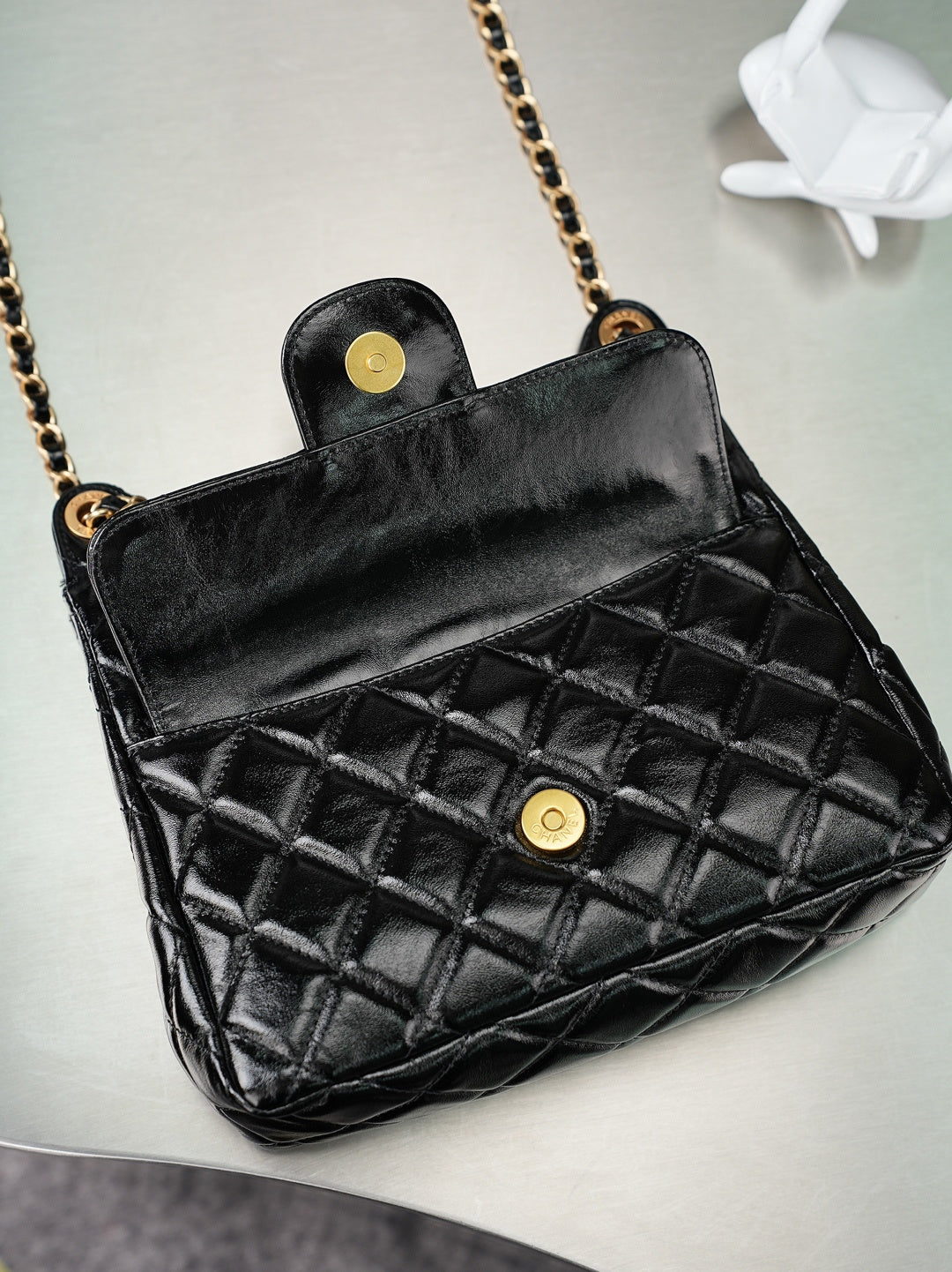 Black quilted Chanel bag with top flap and gold button, gold chain shoulder strap