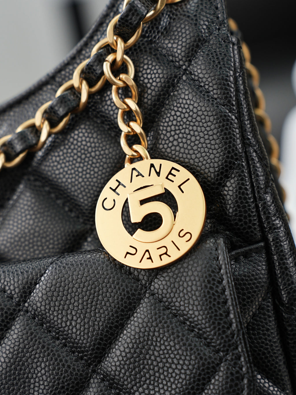 Chanel "5" charm on gold chain attached to dark quilted bag