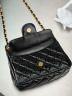 Chanel quilted black bag open with red interior and gold-tone button closure