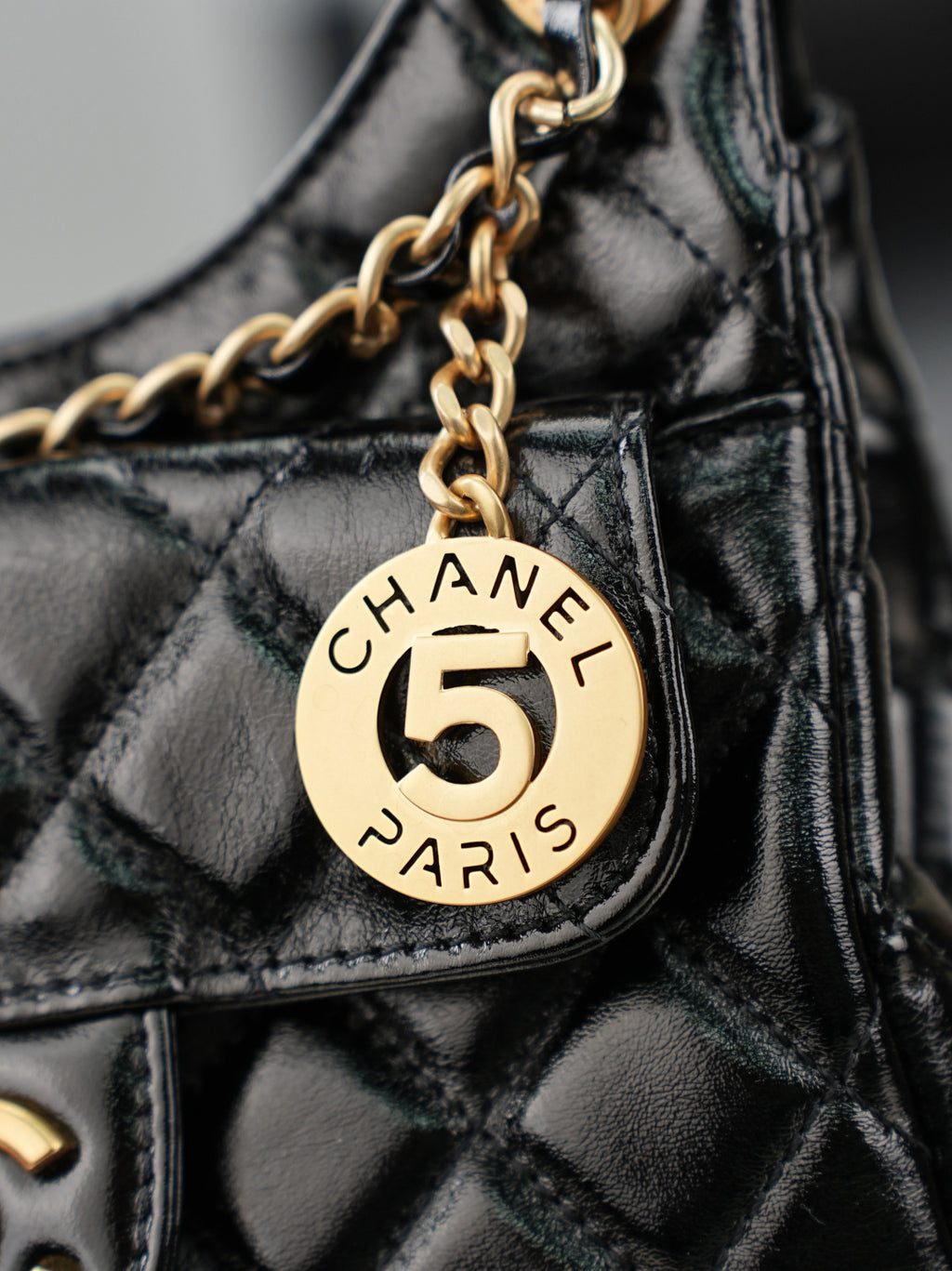 Chanel Paris 5 charm on gold chain attached to quilted black bag