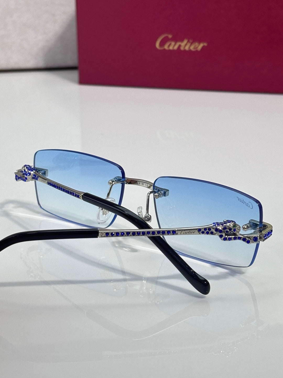 Cartier eyeglasses with light blue lenses, navy temples, and blue rhinestone link details.
